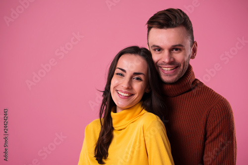 Young cheerful loving couple dressed in sweaters hugging isolated over pink background