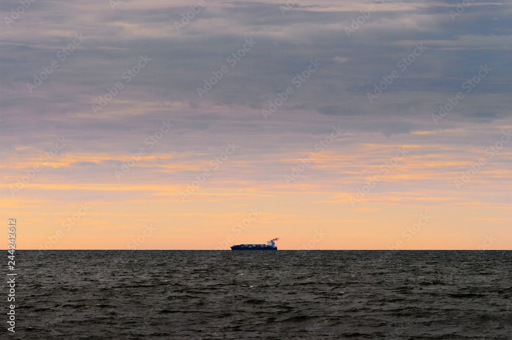 Cargo ship silhouette on the horizon. Container vessel sailing through the Baltic Sea at sunset. Gdansk Bay, Pomerania, Poland.