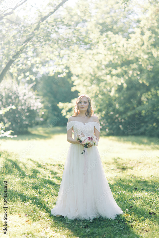The bride in a white dress in nature in the Park. Photo shoot with a bouquet in the style of fine art.