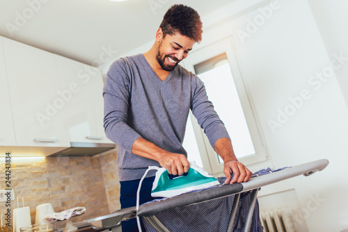 Photography Attractive american black man is ironing shirt at home.