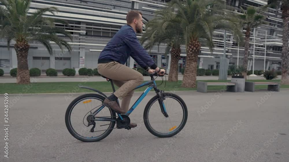 Young bearded man is riding bicycle in park area in summer day, side view Young bearded man is riding bicycle in park area in summer day, side view