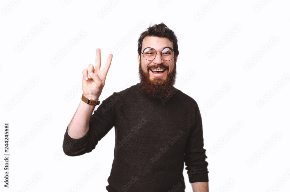 Peace, attractive bearded man in glasses showing victory sign and smiling at the camera Peace, attractive bearded man in glasses showing victory sign and smiling at the camera