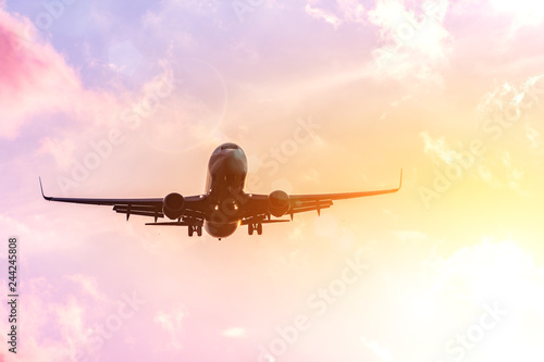 Airplane silhouette in warm in the yellow-pink tones of the sky and clouds. Copcept travel to warmer countries