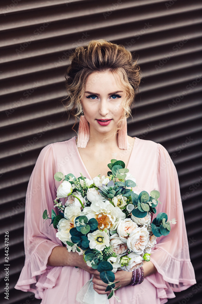attractive young girl in a short dress with a bouquet of flowers posing near the granite wall with rolling shutters. attractive young girl in a short dress with a bouquet of flowers posing near the granite wall with rolling shutters.