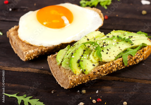 Two different bruschettas with avocado  rucola sesame  seeds  egg on wooden table