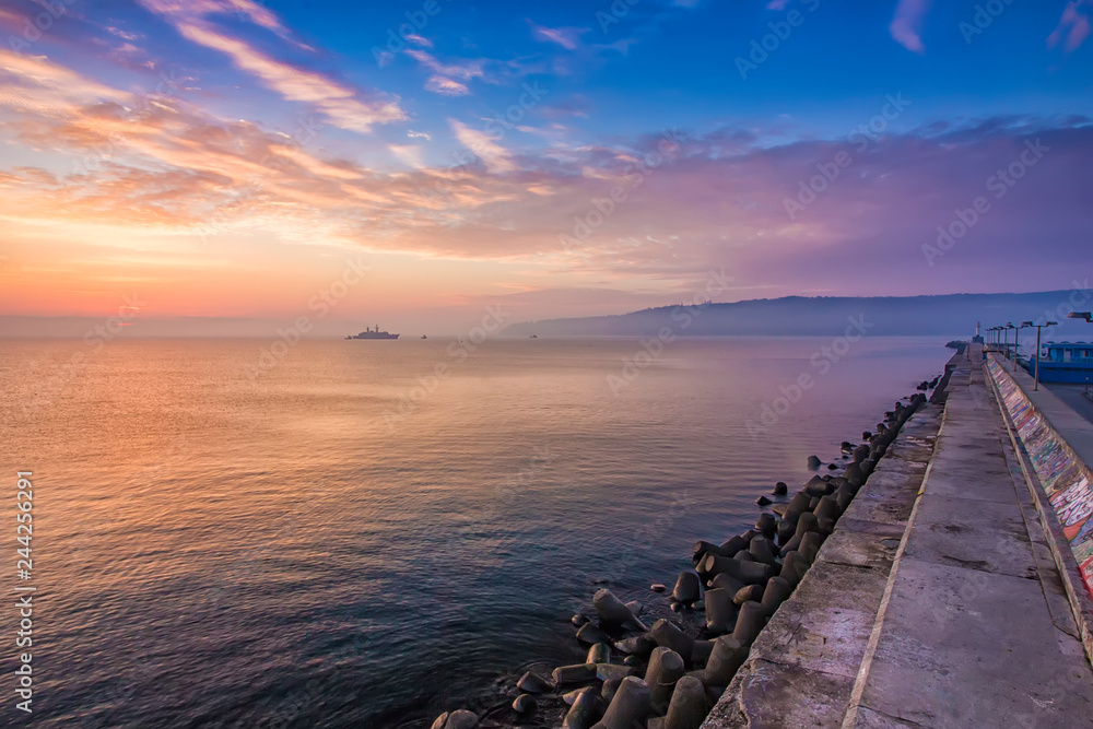 Obraz premium Black sea at a beautiful sunrise, breakwater and ship in the light of the rising sun, Varna, Bulgaria