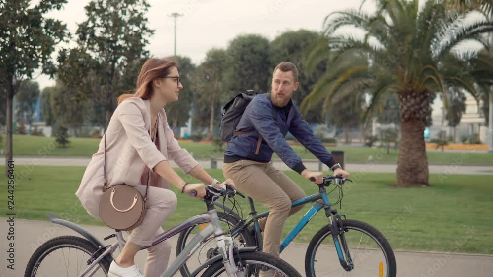 Cheerful male and female bicyclists are chatting happily in walking in city park Cheerful male and female bicyclists are chatting happily in walking in city park