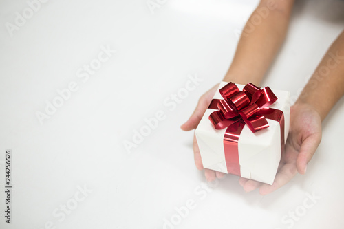 Fototapeta Naklejka Na Ścianę i Meble -  The children's hands holding craft paper gift box with as a present for Christmas, new year, valentine day or anniversary on white background, top view