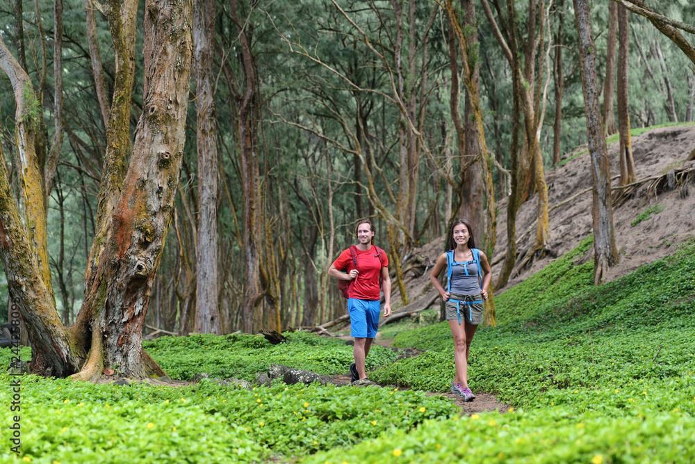 Hiking couple tourists walking together in forest trail path in summer travel vacation destination in Hawaii. Nature rainforest landscape, happy hikers people with backpacks. Hiking couple tourists walking together in forest trail path in summer travel vacation destination in Hawaii. Nature rainforest landscape, happy hikers people with backpacks.