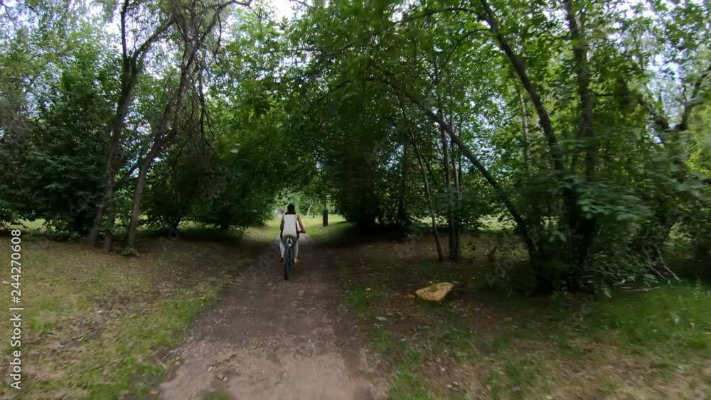 Cycling in the park. Girl riding a bike on a forest trail. Back view. Slow motion Cycling in the park. Girl riding a bike on a forest trail. Back view. Slow motion