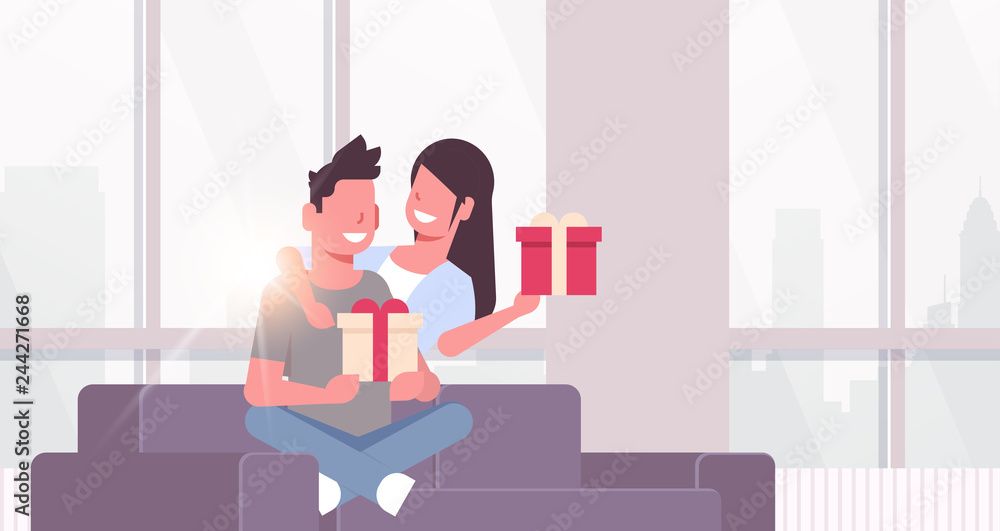 couple holding present wrapped gift boxes man woman embracing sitting couch celebrating holiday concept happy lovers modern living room interior horizontal