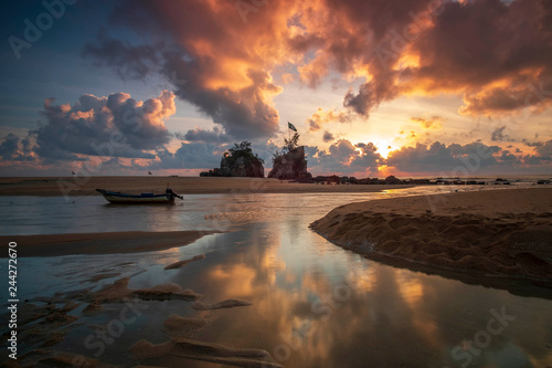 Reflection of dramatic clouds and two standing rocks near the sea with stranded boat.