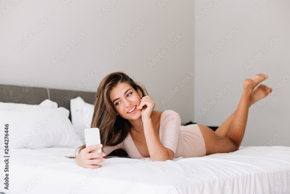 Attractive young girl taking selfie on phone on bed in apartment in the morning Attractive young girl taking selfie on phone on bed in apartment in the morning