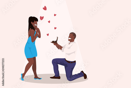 man kneeling holding engagement ring proposing to surprised woman marry him happy valentines day concept african couple in love marriage offer full length horizontal