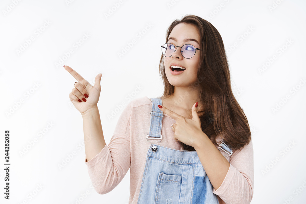 Charming girl turning attention at upper left corner, pointing with finger pistols open mouth from amazement and looking impressed and curious at awesome advertisement over gray background Charming girl turning attention at upper left corner, pointing with finger pistols open mouth from amazement and looking impressed and curious at awesome advertisement over gray background