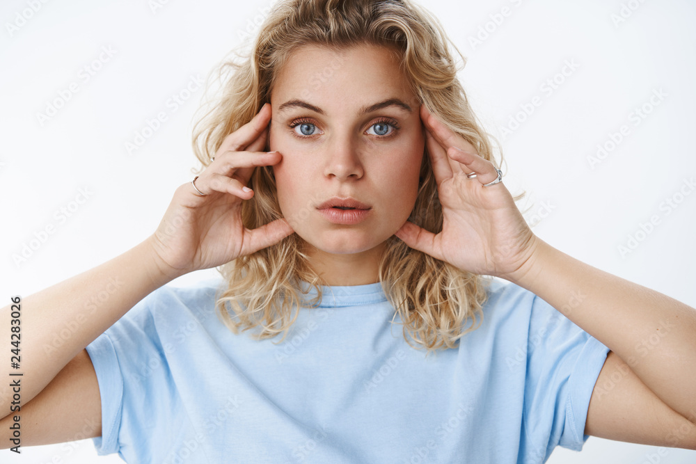 Cose-up shot of sensual and feminine serious-looking blond girl with short curly haircut holding hands on face and looking focused at camera with determined gaze concern about aging or skin Cose-up shot of sensual and feminine serious-looking blond girl with short curly haircut holding hands on face and looking focused at camera with determined gaze concern about aging or skin