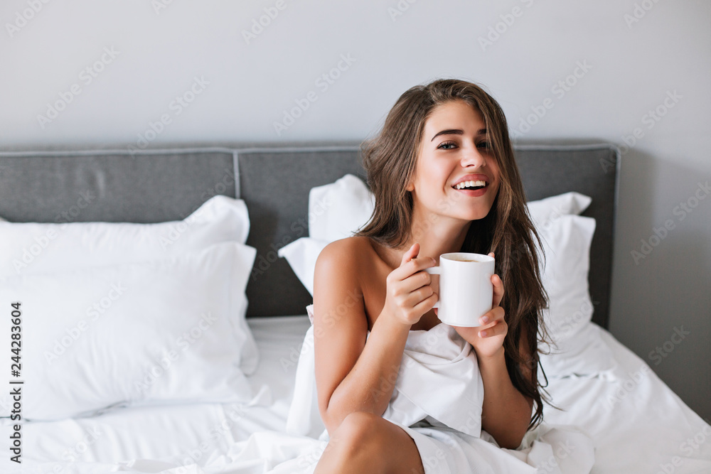 Portrait pretty girl with naughty shoulders drinking coffee on bed in the morning in apartment Portrait pretty girl with naughty shoulders drinking coffee on bed in the morning in apartment