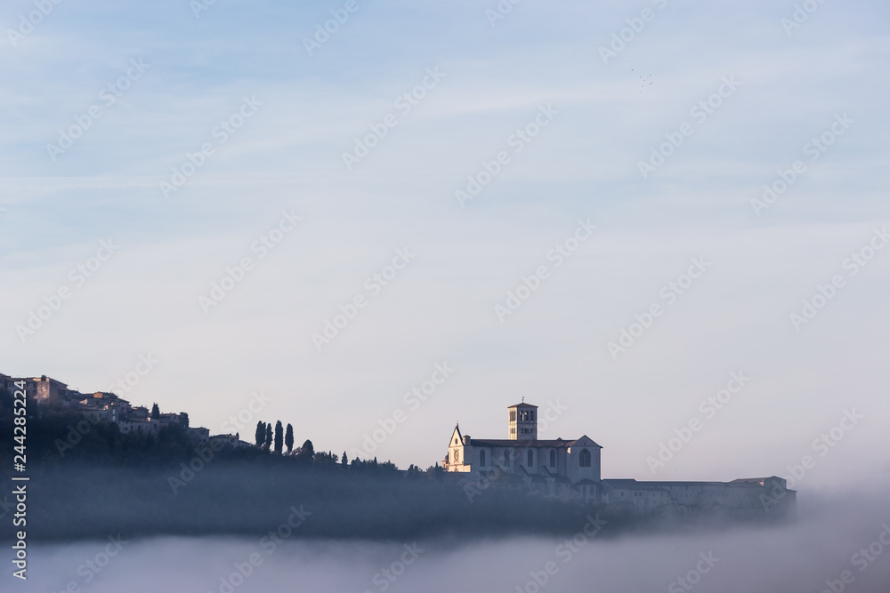 A view of St.Francis church in Assisi in the middle of mist beneath a blue sky with clouds