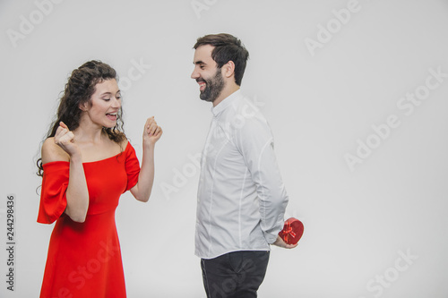 Young couple loving. A man made a present for his wife. During this time, the red field is presented in the form of a heart. Wife is pleasantly surprised. Dressed in a red dress and a white shirt.