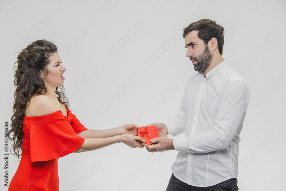 Young couple loving. A man made a present for his wife. During this time, the red field is presented in the form of a heart. Wife is pleasantly surprised. Dressed in a red dress and a white shirt. Young couple loving. A man made a present for his wife. During this time, the red field is presented in the form of a heart. Wife is pleasantly surprised. Dressed in a red dress and a white shirt.