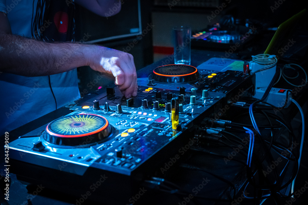 Naklejka premium DJ music console and laptops in bright colors of light in night club bright blue background