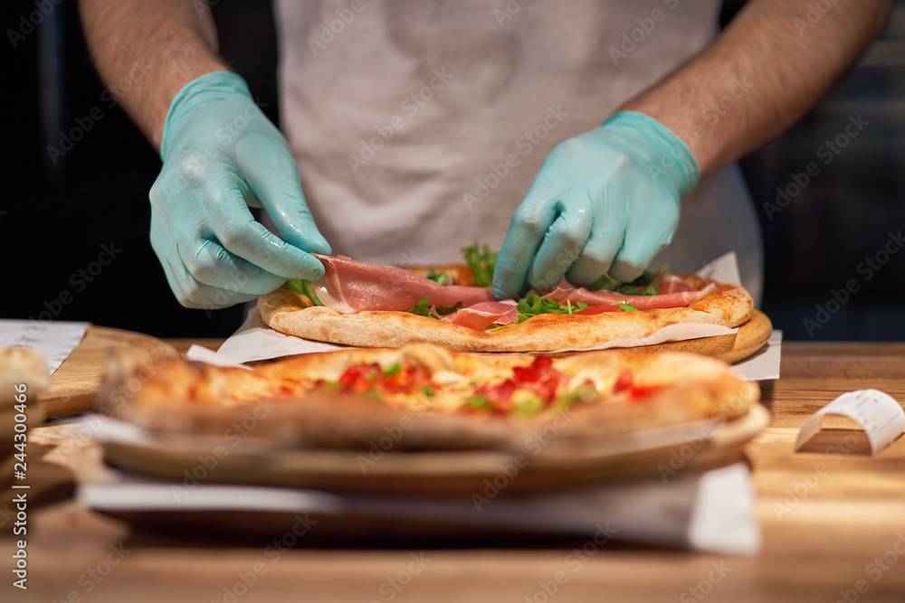 Chef making a parma or prosciutto ham Italian pizza in a close up view of his hands placing the meat