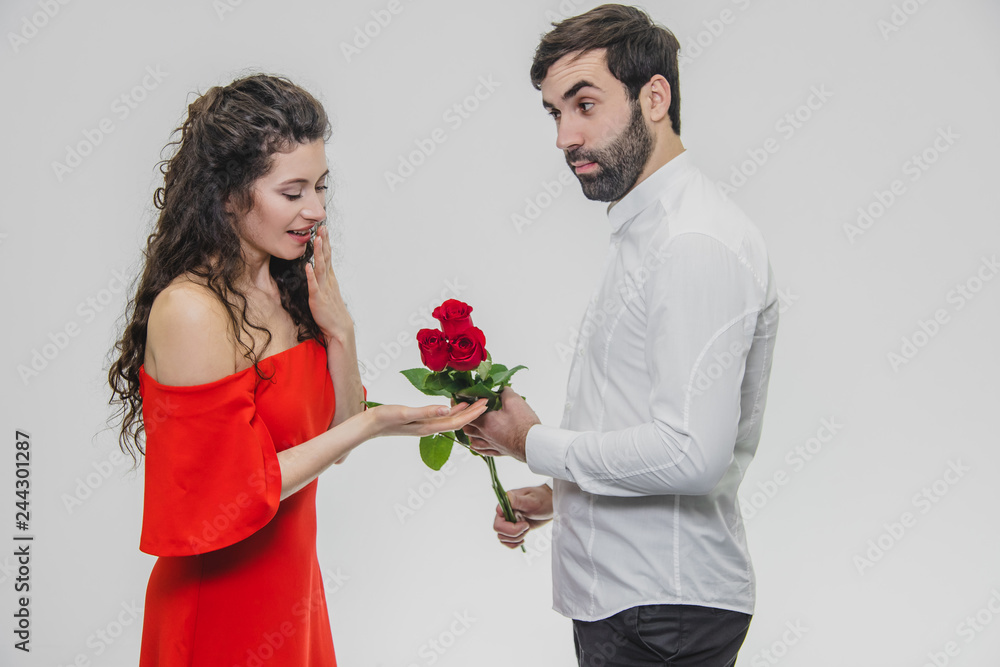 A young man hiding a bunch of roses behind his surprise to astonish his girlfriend for Valentine's Day. Dressed in red dress and white shirt. A young man hiding a bunch of roses behind his surprise to astonish his girlfriend for Valentine's Day. Dressed in red dress and white shirt.