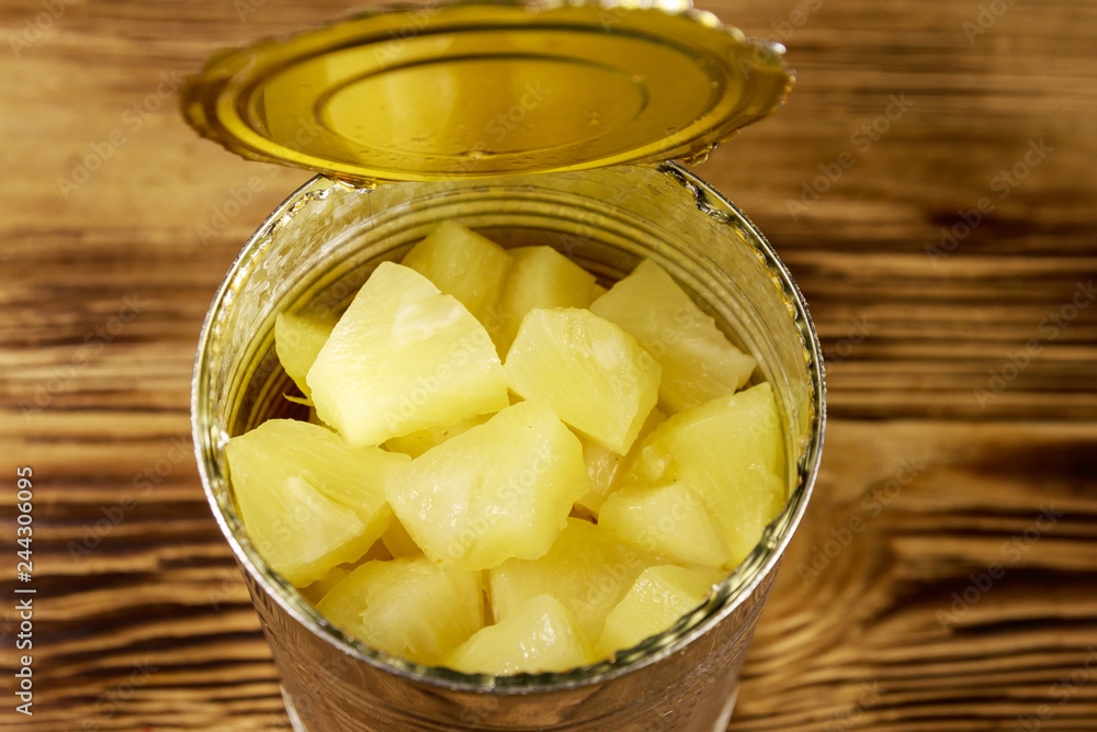 Opened tin can of pineapple pieces on wooden table Opened tin can of pineapple pieces on wooden table