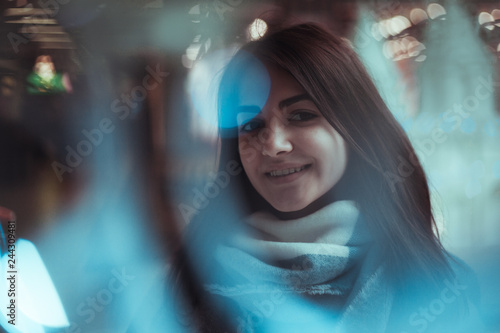 unusual portrait of positive young girl through blue fair lights in the mall. Big light bokehs on foreground