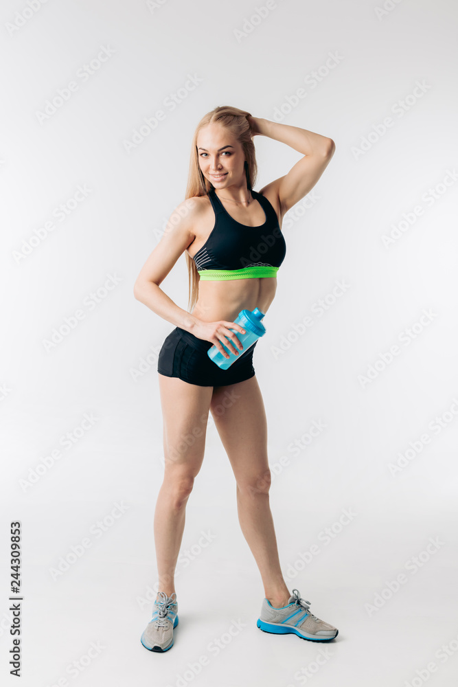 happy good looking fair-haired girl in fashionable sportswear touching her head and holding cold drink. fresh drink after training . isolated white background happy good looking fair-haired girl in fashionable sportswear touching her head and holding cold drink. fresh drink after training . isolated white background