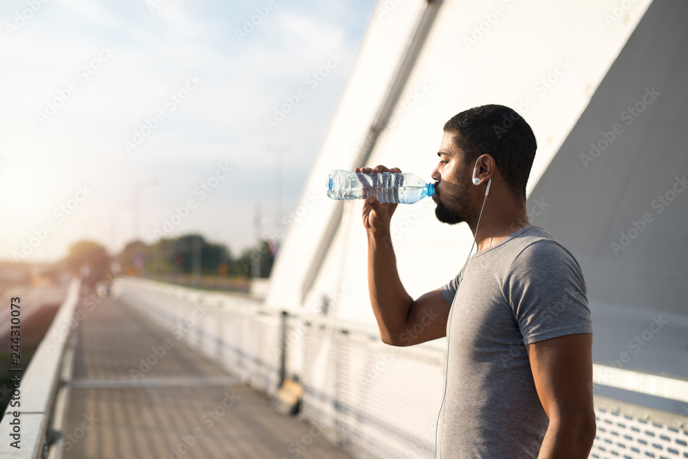 Young attractive sporty man drinking water and hydrating body after training. Athlete refreshing himself.