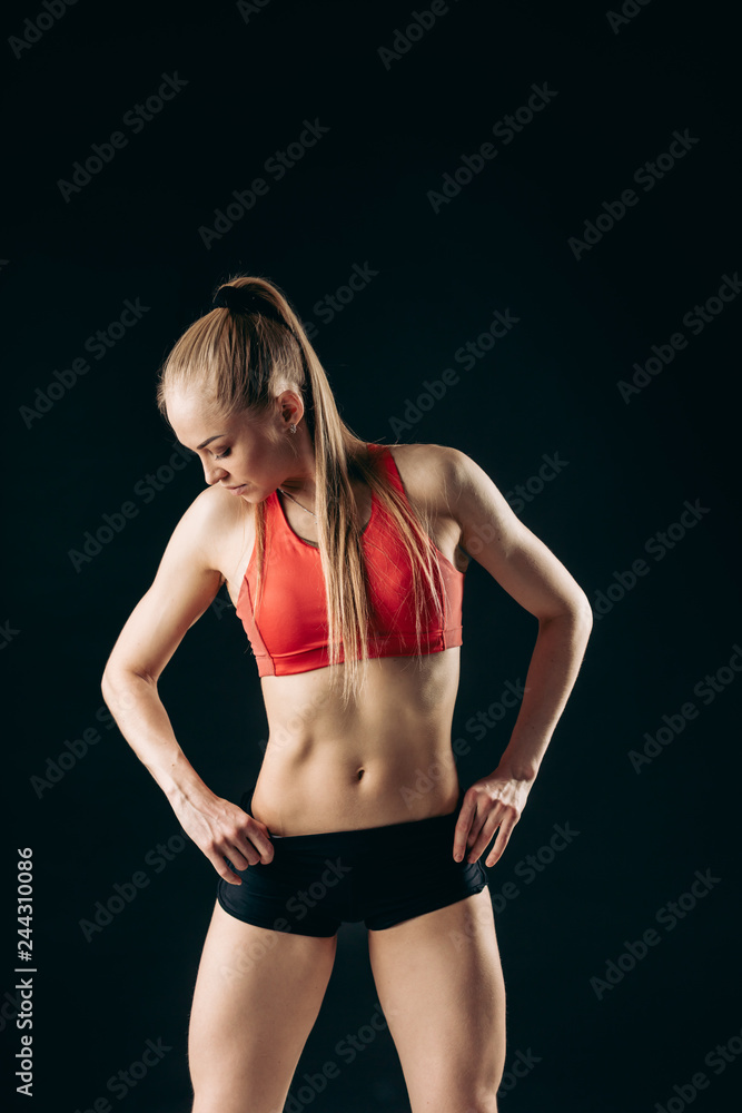 Fototapeta premium Muscular slender stylish girl standing looking down with her hands on hips on black background.close up shot.