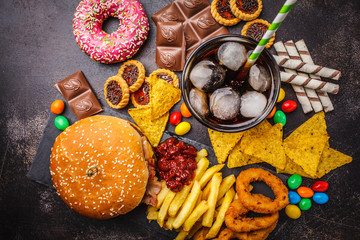 Junk food concept. Unhealthy food background. Fast food and sugar. Burger, sweets, chips, chocolate, donuts, soda, top view.