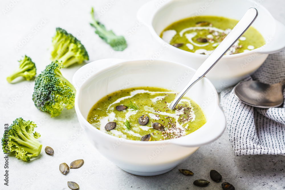Vegan detox broccoli cream soup with coconut cream and pumpkin seeds in white bowl, copy space. Vegan detox broccoli cream soup with coconut cream and pumpkin seeds in white bowl, copy space.