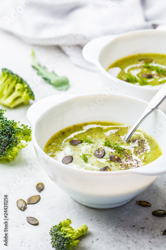 Vegan detox broccoli cream soup with coconut cream and pumpkin seeds in white bowl, copy space.