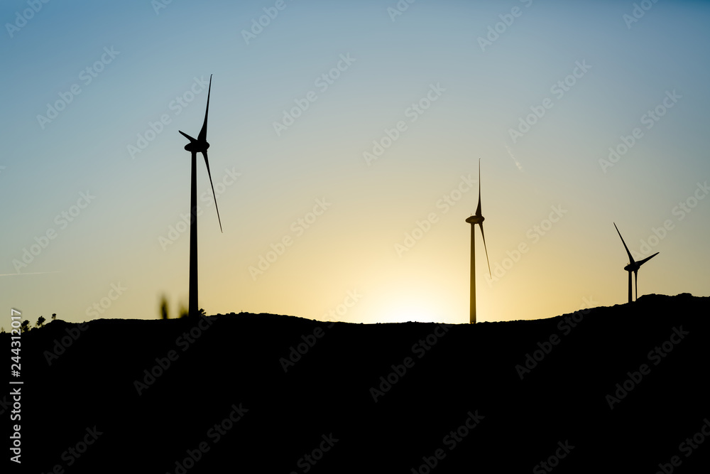 Silhouette view of a wind turbines on top of mountains, sunset sky Silhouette view of a wind turbines on top of mountains, sunset sky