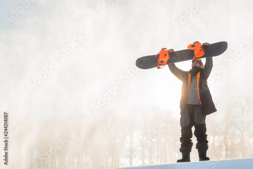 serious snowboarder checking his snowboard before descending. full length photo. copy space. sporty fit man is holding a snowboard over the head and looking at it