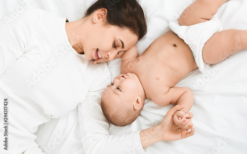 Happy mother and her cute little newborn baby lying on bed
