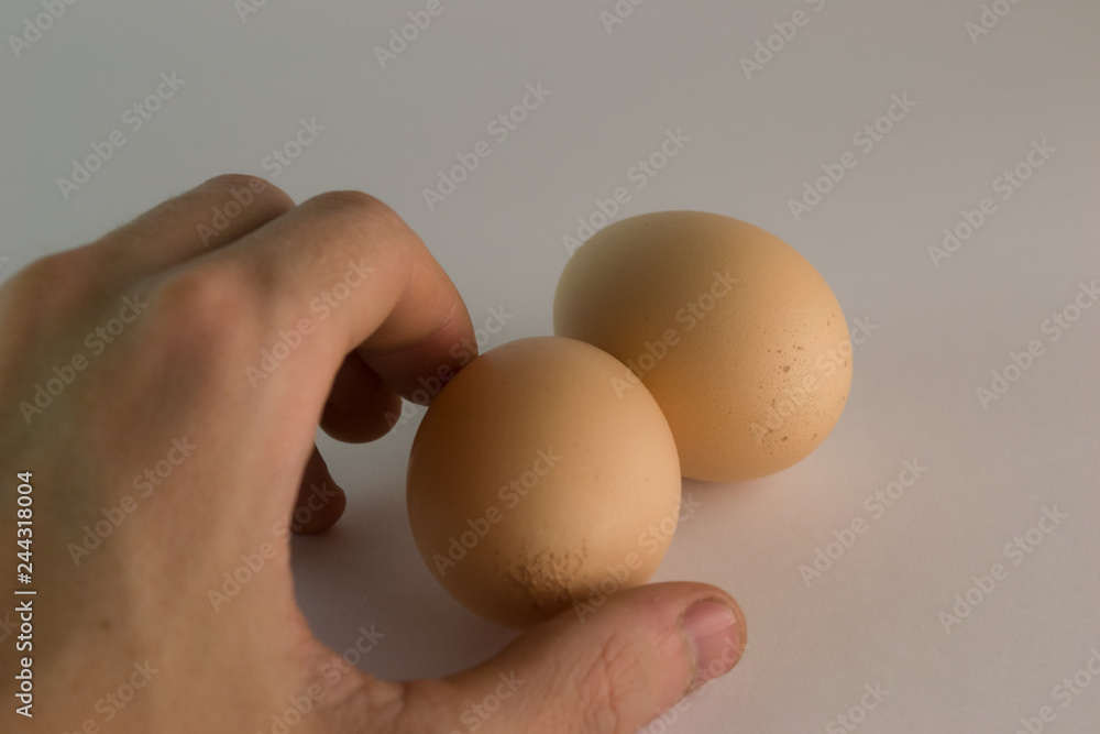A man takes one of two chicken eggs with two fingers of his left hand. A man takes one of two chicken eggs with two fingers of his left hand.