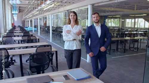 employees stop in front of the camera looking with successful smile two young white-collar workers walking around the office