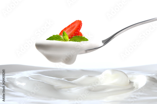 Plain yogurt on a spoon with fresh strawberry on top hanging above of plain yogurt isolated on white background