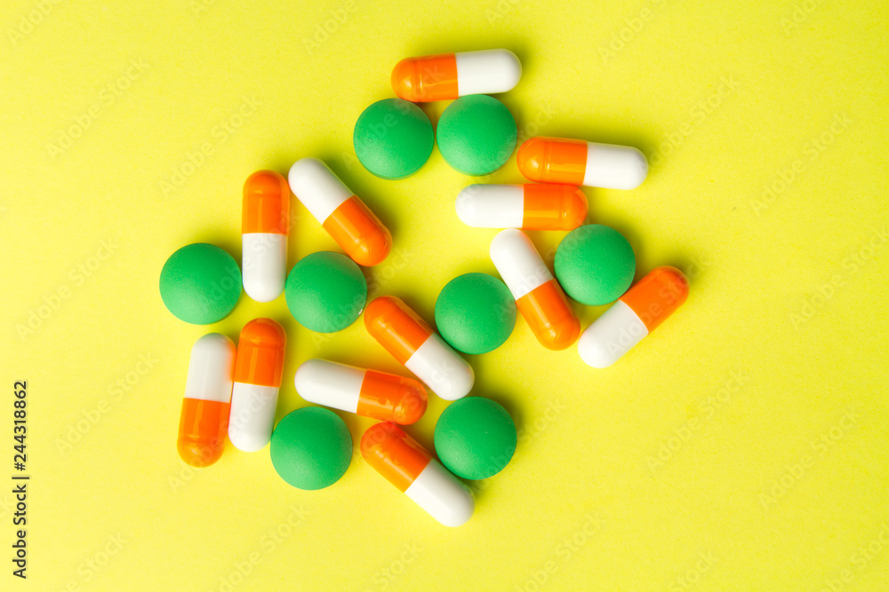 Medicine green pills and orange capsules on yellow background with copy space. Drug prescription for treatment medicine. Medical background, template