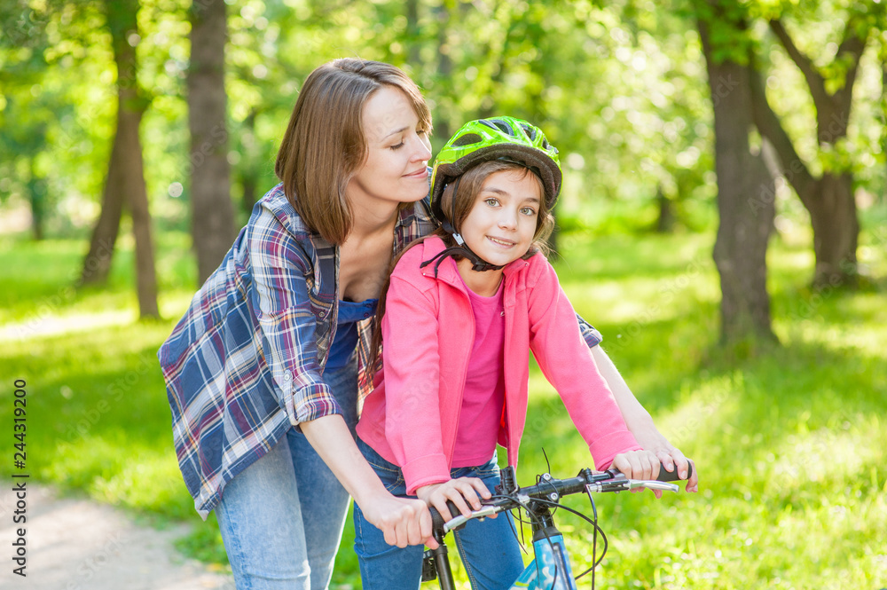 Happy family. Mother teaches her daughter to ride a bicycle in the park