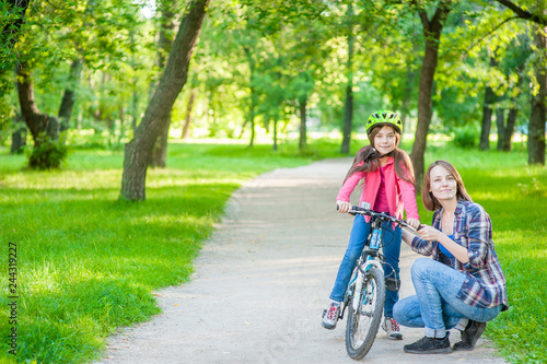 portrait of mom and daughter with a bicycle in the park. Empty space for text