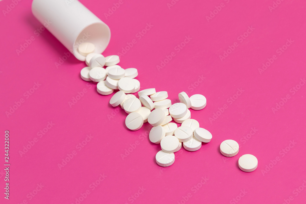 Circle pills tablets spilling out of a white plastic medicine bottle on pink background Circle pills tablets spilling out of a white plastic medicine bottle on pink background