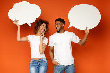 Young black couple holding speech bubbles on orange background