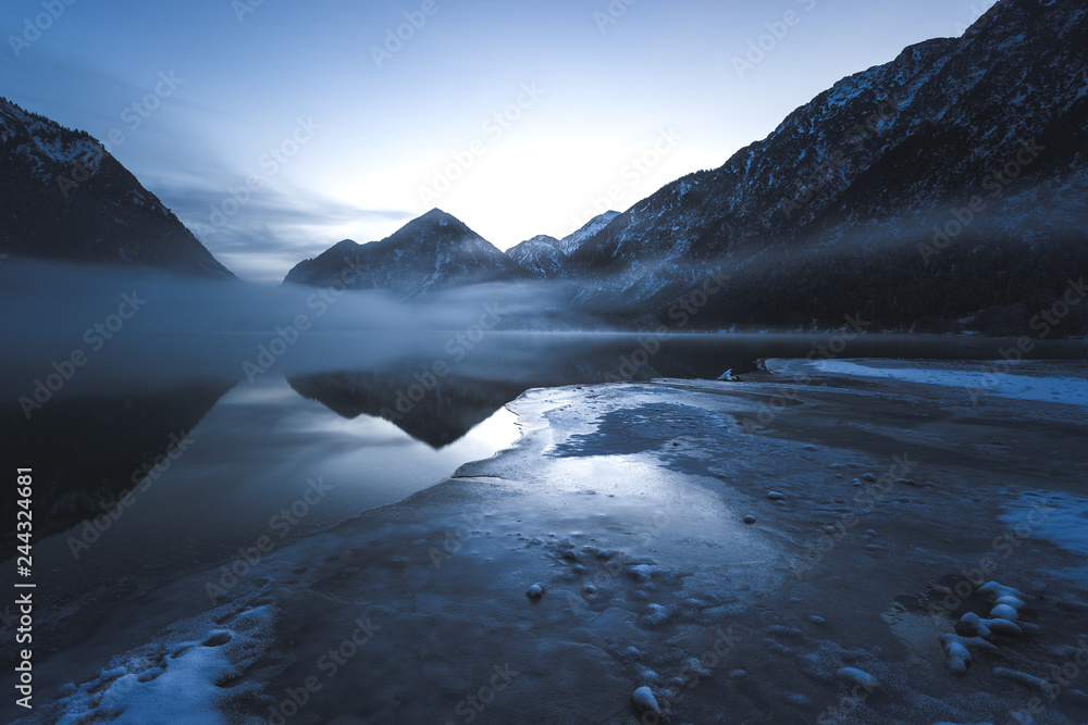 Winterliches Alpenpanorama mit Spiegelung und Nebel am See im Winter, Heiterwanger See, Tirol, Österreich