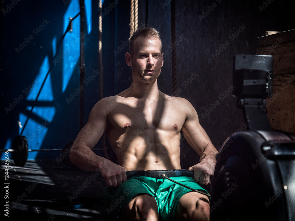 Muscular young shirtless man, training back on equipment, pulling cable ...