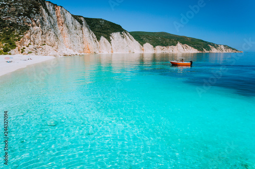 Fototapeta Naklejka Na Ścianę i Meble -  Small red boat on clear blue sea water near to amazing beach on mediterranean island. Summer beach vacation relaxation concept