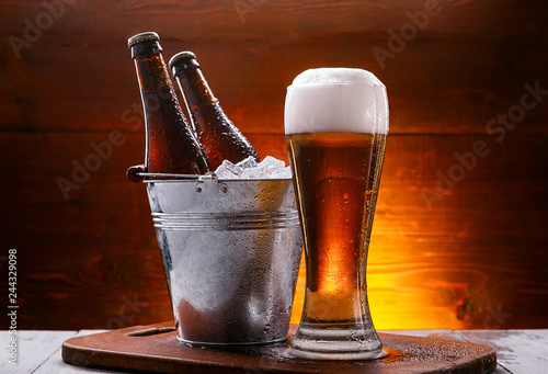 two bottles of beer in a bucket with ice and a glass of beer with lush foam next to a dark background photo